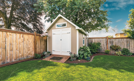 small storage shed, green grass, trees, blue sky, fence